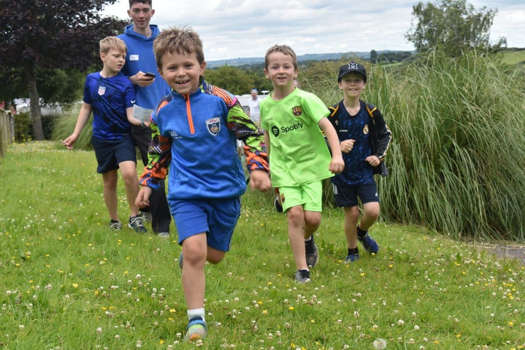 Kids running outdoors through green grass smiling.