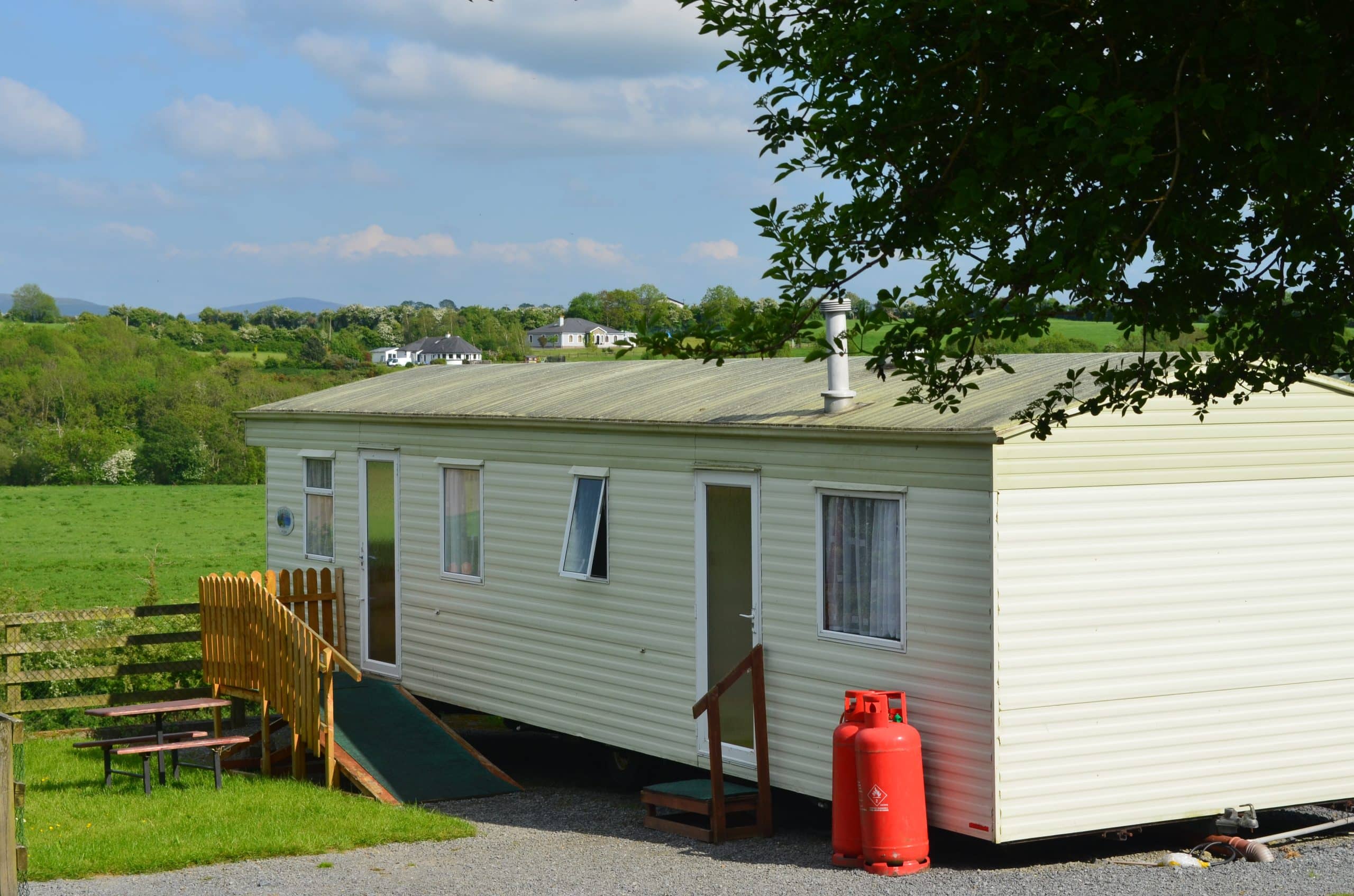 Mobile home beside green field with trees in the distance.
