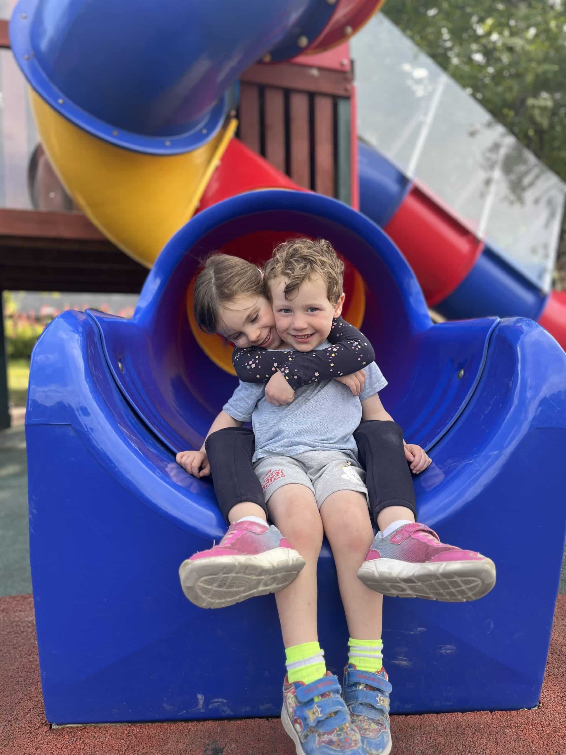 Two kids seated on a playground slide, laughing and playing in Nore Valley.