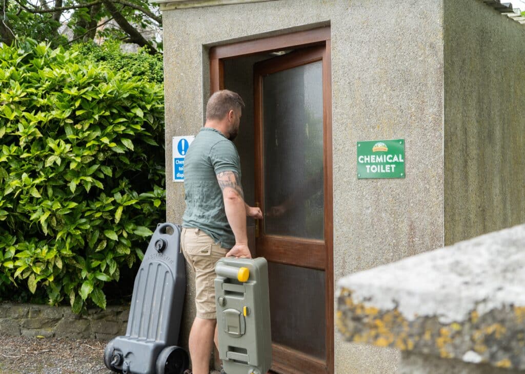 A man carrying a chemical toilet from a caravan to empty it into the chemical disposal toilet on the campsite